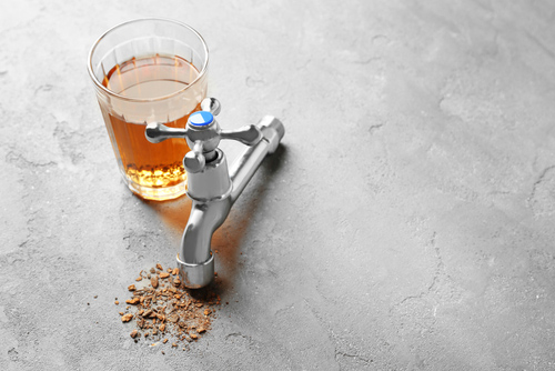 Brown water in a glass next to a disconnected faucet that is rusty