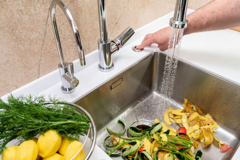 Man's hand turning on a garbage disposal to remove food waste from kitchen sink