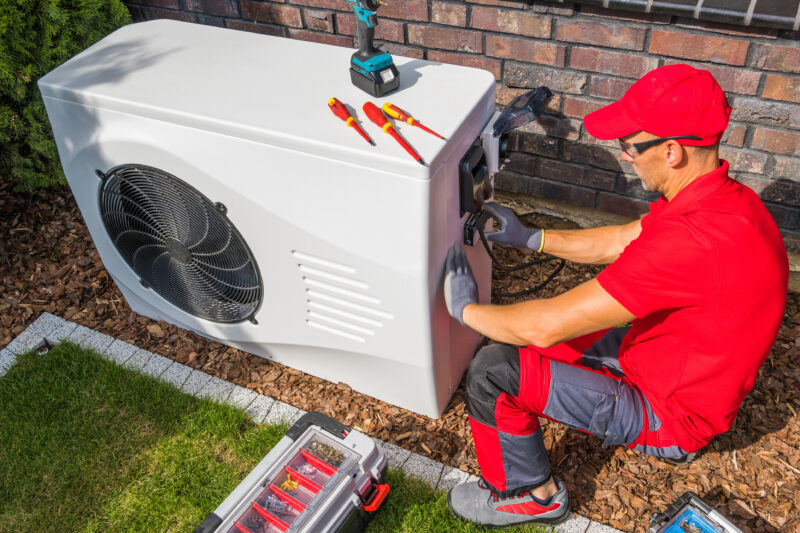 Professional HVAC technician in red uniform performing a tune-up modern heat pump unit