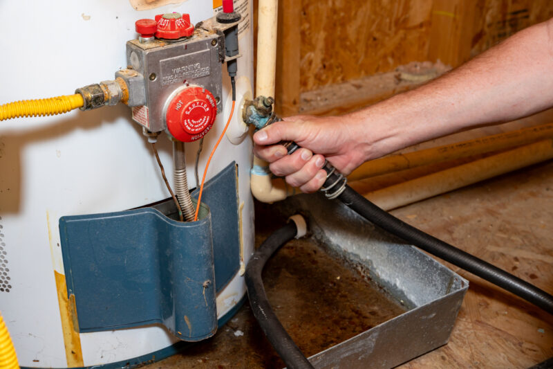 Plumber's hand connecting drain hose to water heater